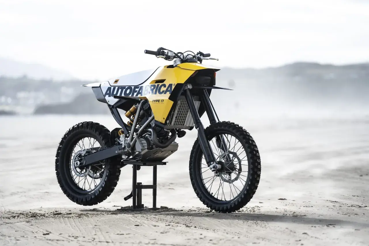 Żółto-biały motocykl customowy Autofabrica Type 17, bazujący na BMW G450X, stoi na plaży.