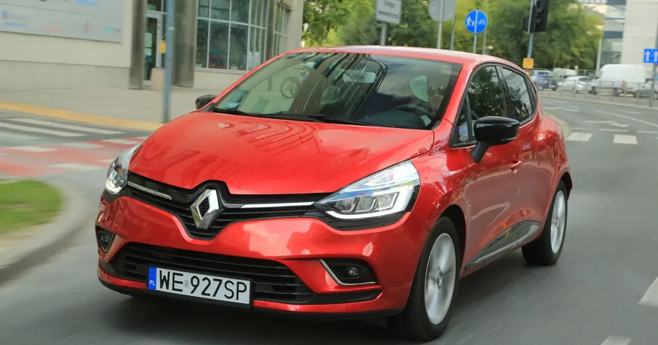 Czerwony Renault Clio 3 1.2 benzyna w ruchu miejskim. Kierowca w okularach przeciwsłonecznych.