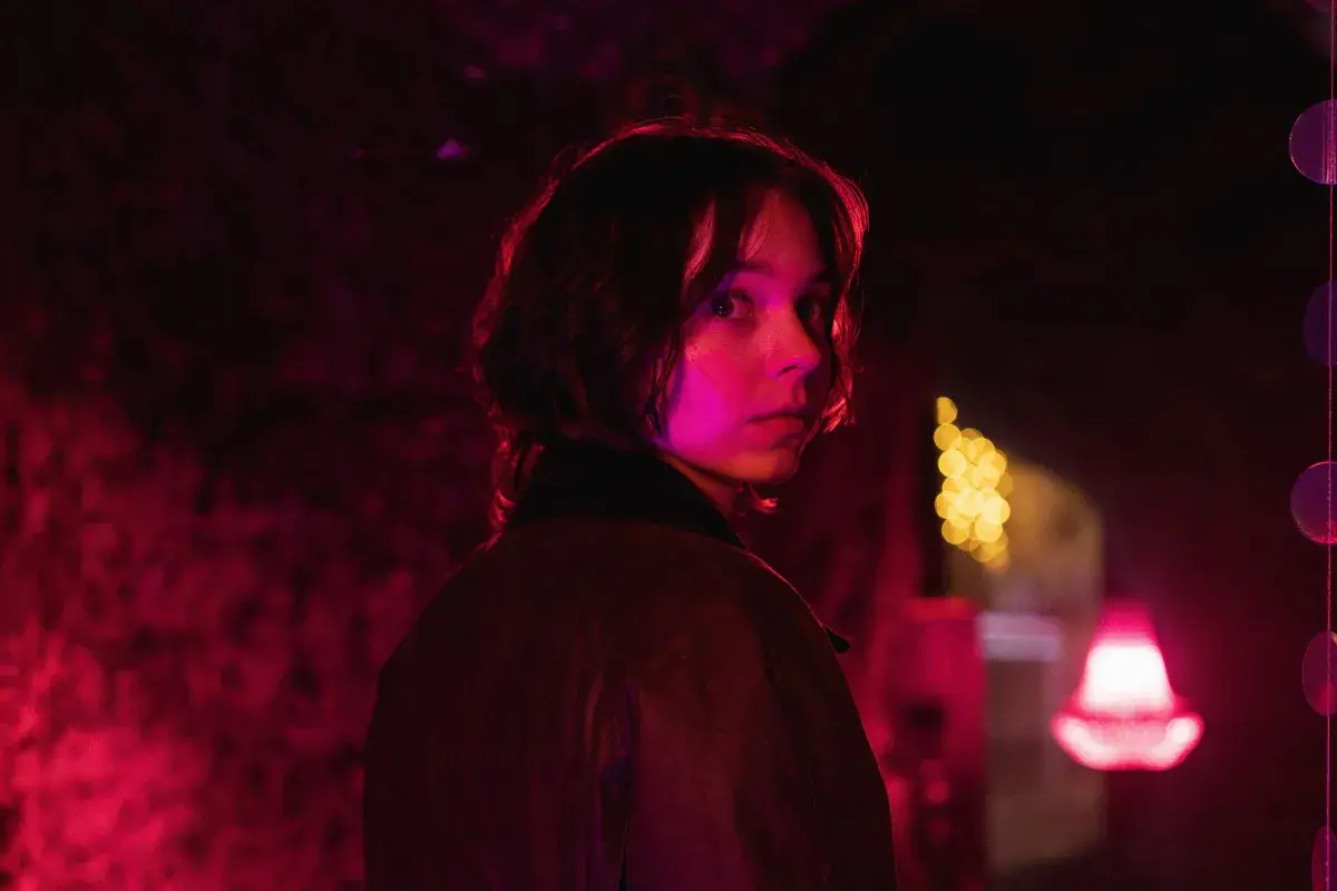Młoda kobieta z zaciekawieniem spogląda przez ramię w mrocznym, neonowym otoczeniu. Czy to scena z nowego serialu Netflix?