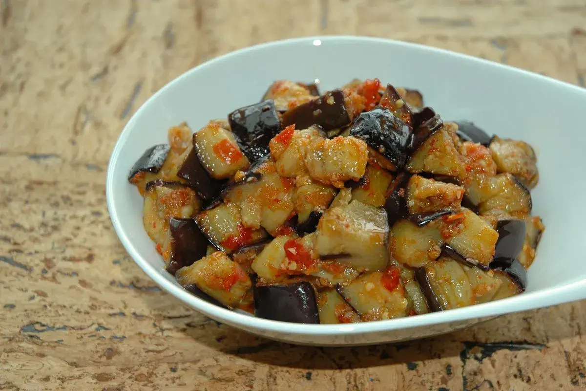 Melanzane al microonde, tagliate a cubetti e condite con pomodoro e spezie, servite in una ciotola bianca.