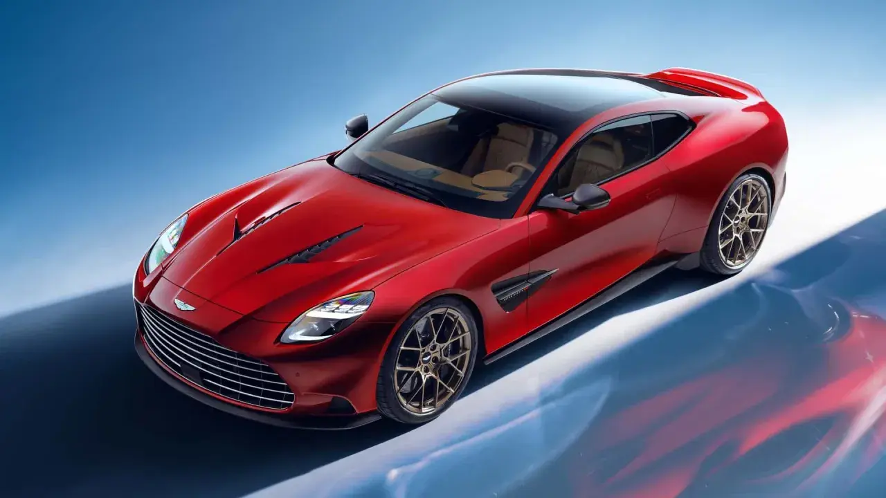 Czerwony Aston Martin Vanquish z brązowym wnętrzem i czarnym dachem, prezentujący swoje sportowe linie na tle błękitnego nieba.
