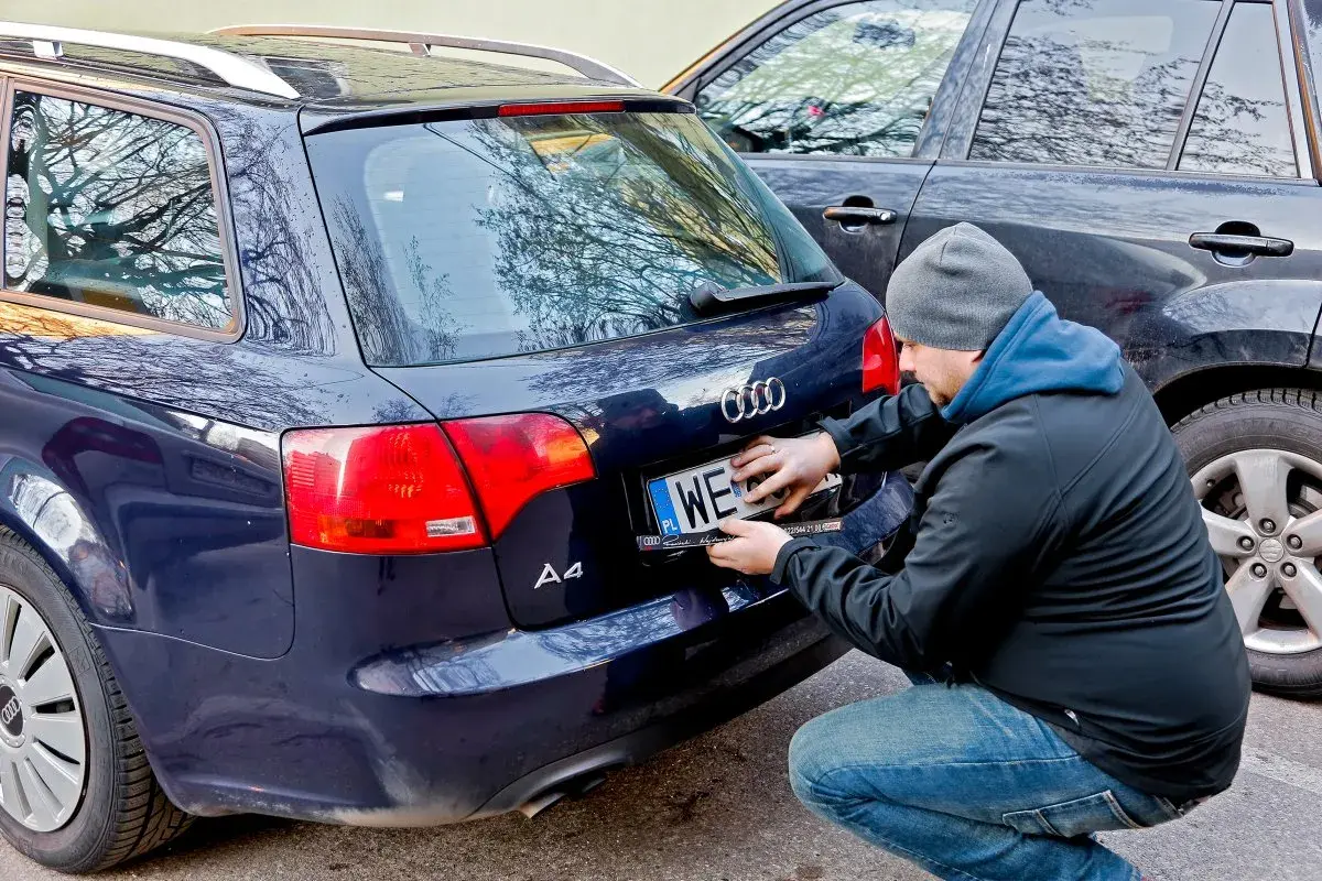 Mężczyzna montuje tablicę rejestracyjną na samochodzie Audi A4. Nowa rrs rejestracja gotowa do drogi.