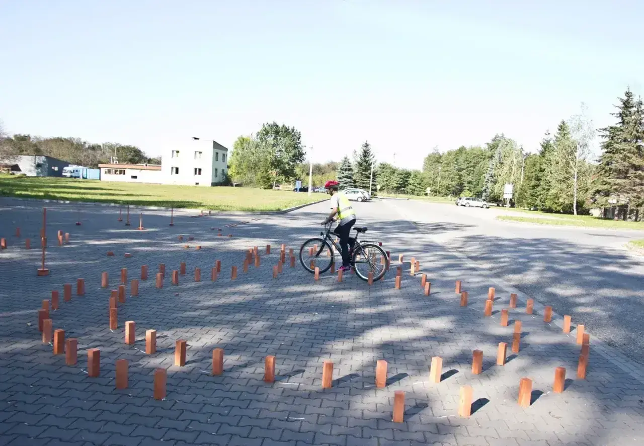 Młody rowerzysta w kamizelce odblaskowej i kasku pokonuje tor przeszkód z palików, przygotowując się do egzaminu na kartę rowerową.