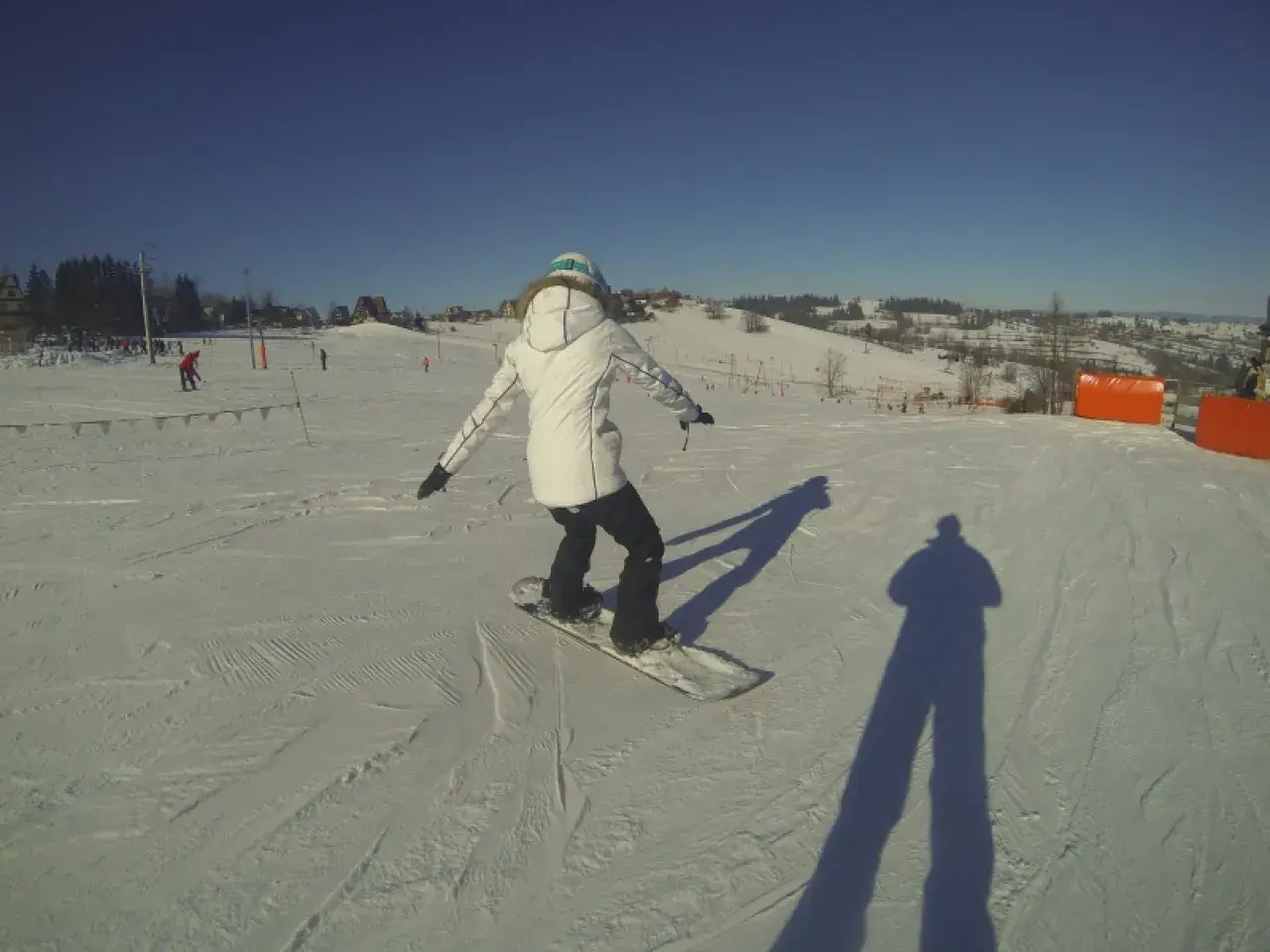 Osoba na snowboardzie na stoku narciarskim, ucząca się w szkole narciarskiej Budzyńskich. Słoneczny dzień, czyste niebo.