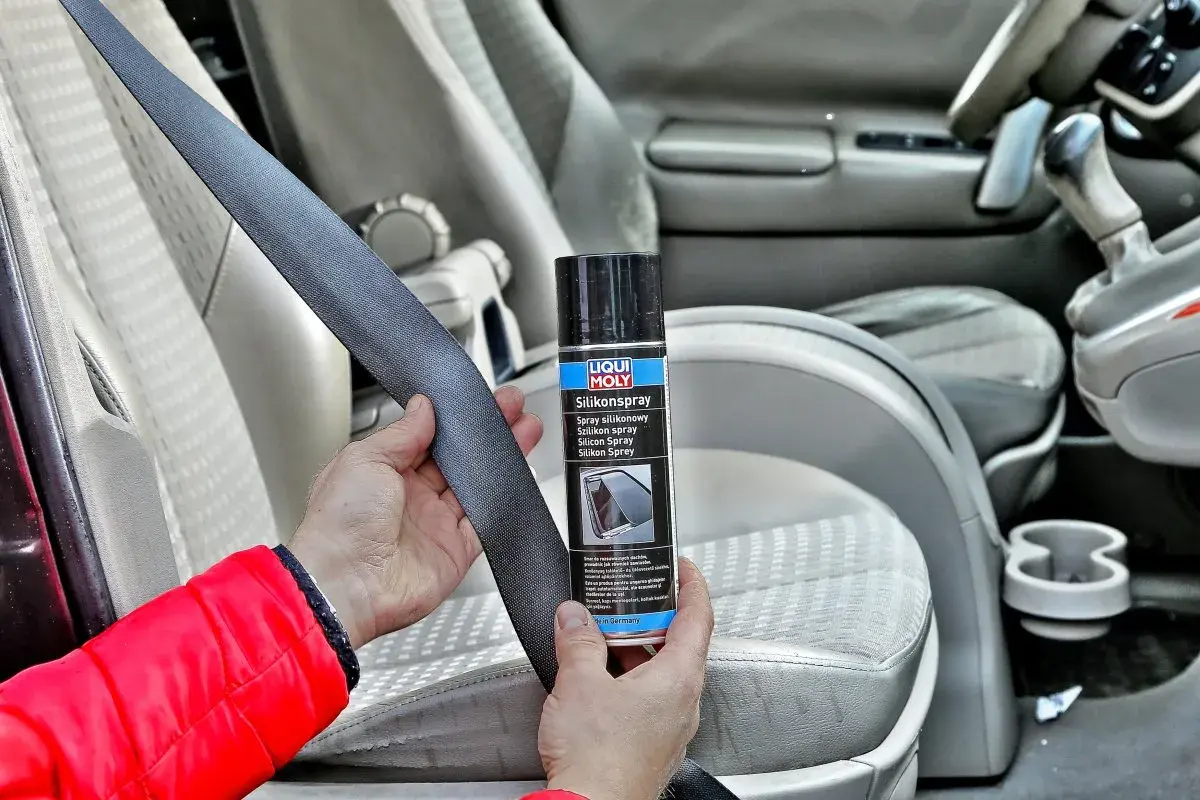 Ręce trzymają pas bezpieczeństwa i puszkę z napisem "Silikonspray". Dowiedz się, jak usunąć silikon z materiału w samochodzie.