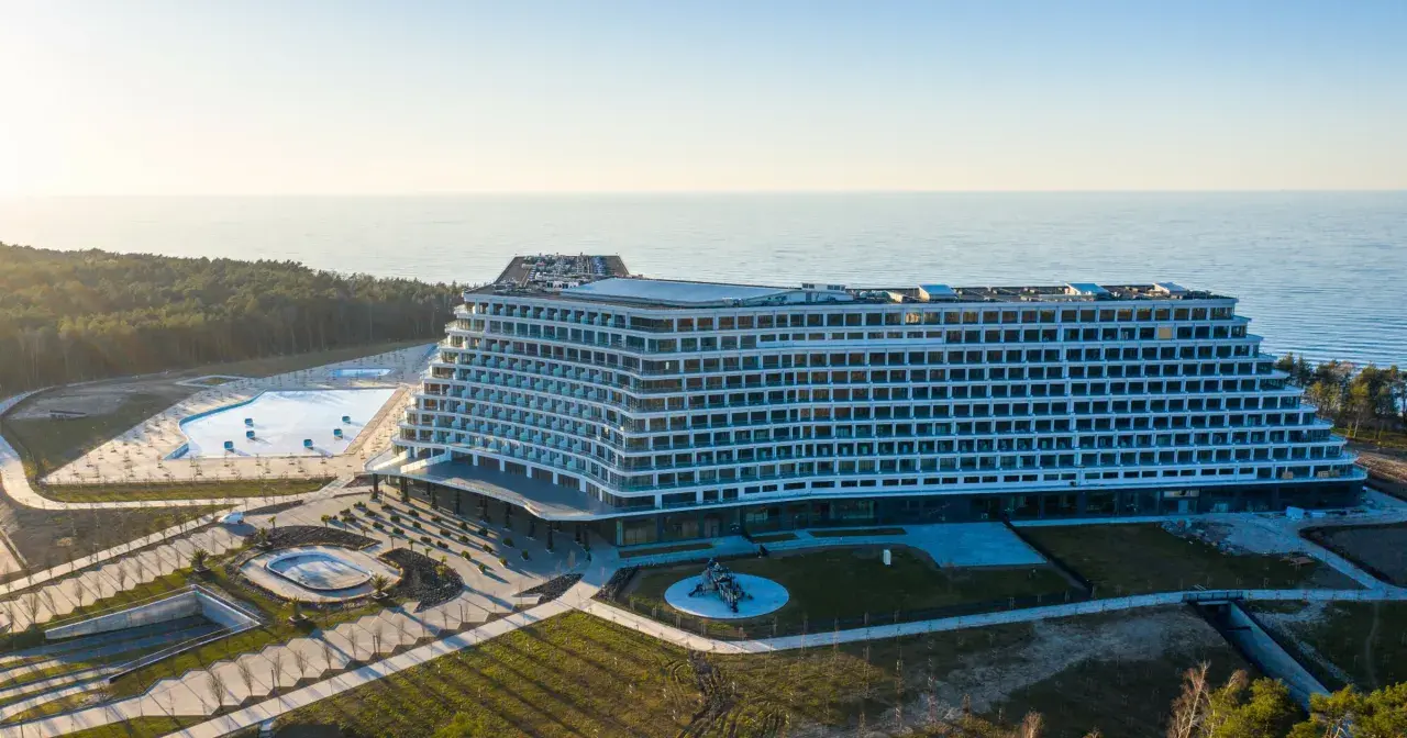Nowoczesny, falisty pobierowo nowy hotel z basenami i widokiem na morze, otoczony lasem.