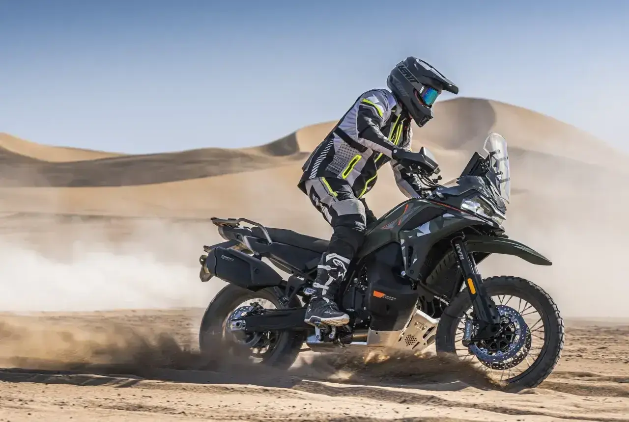 Motocyklista w pełnym rynsztunku szaleje na pustyni na swoim KTM 790 Adventure, wzbijając tumany piasku.