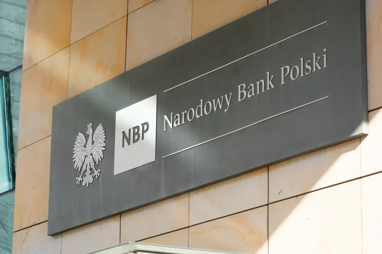 Tablica z godłem Polski i napisem "NBP Narodowy Bank Polski". Decyzje NBP wpływają na obniżkę stopy procentowej.