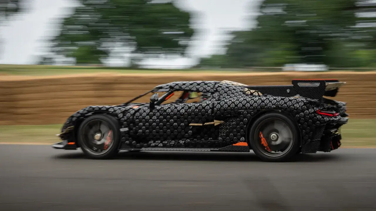 Czarny, pikselowy hypercar z pomarańczowymi akcentami pędzi po torze, tworząc wrażenie ruchu.