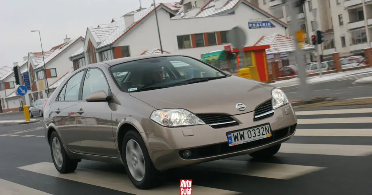 Brązowy Nissan Primera przejeżdża przez pasy na tle zaśnieżonych domów.