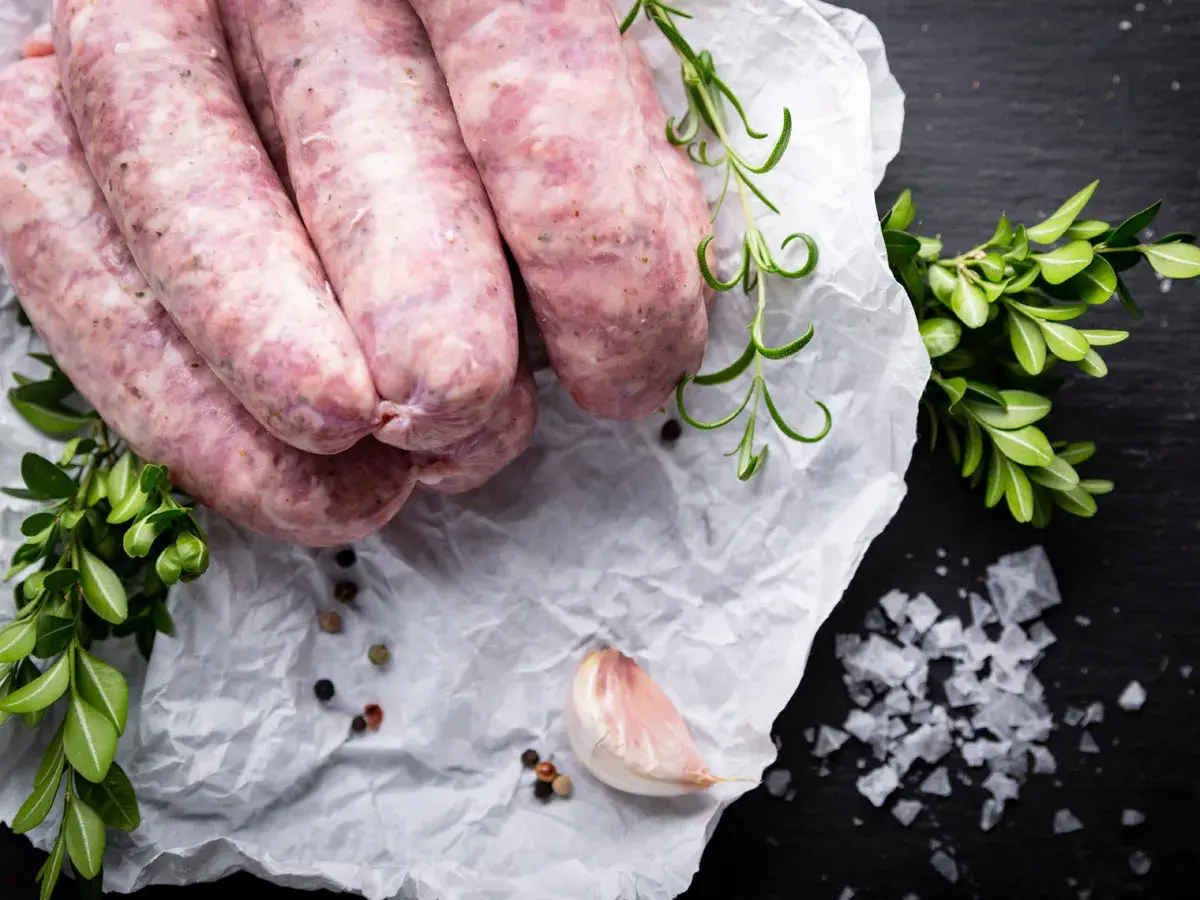 Surowa biała kiełbasa na papierze, obok gałązki rozmarynu i czosnek. Zastanawiasz się nad biała kiełbasa kcal?
