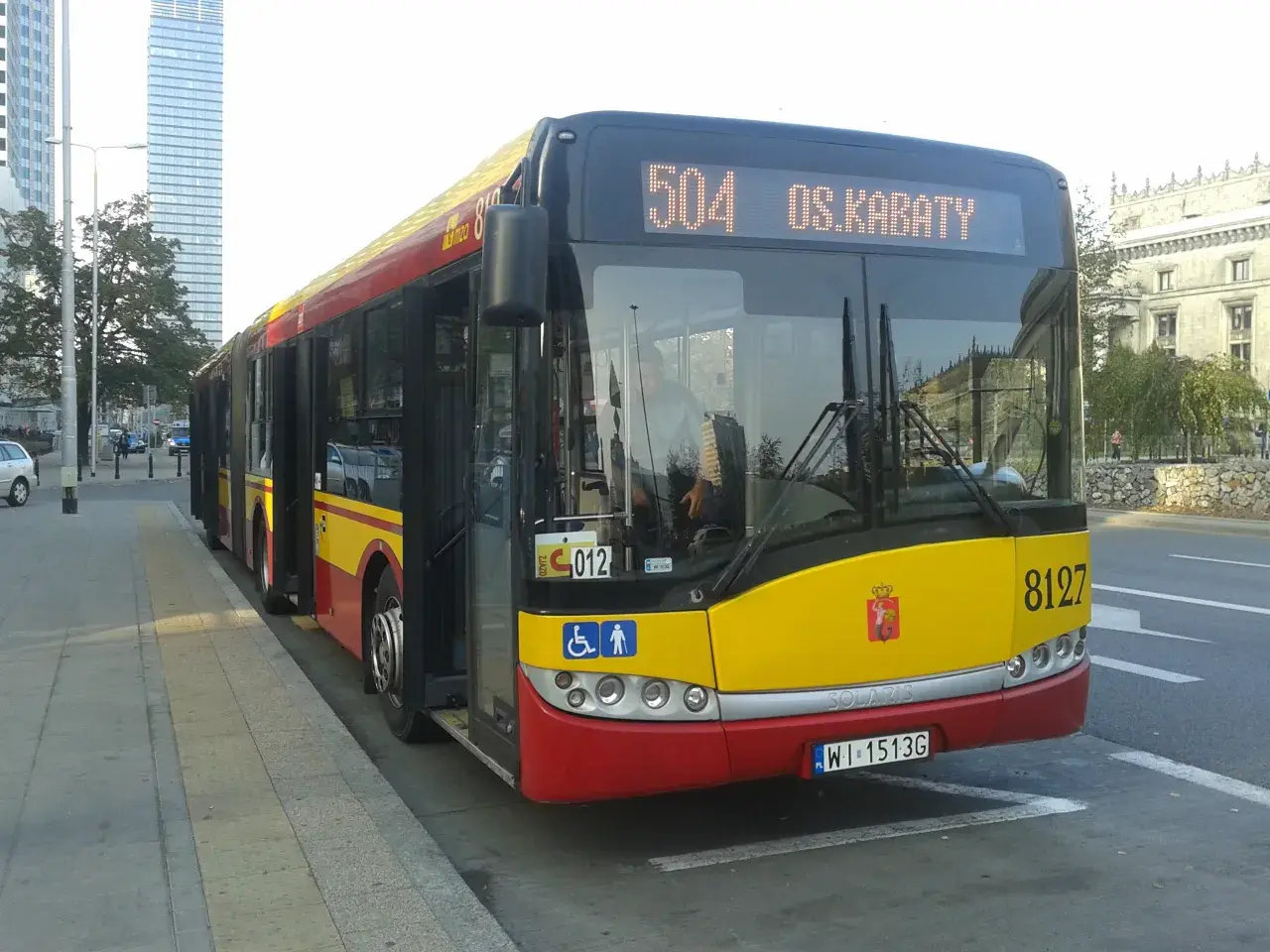 Autobus 504 OS.KABATY z numerem bocznym 8127 stoi na przystanku. W tle widać nowoczesne budynki.