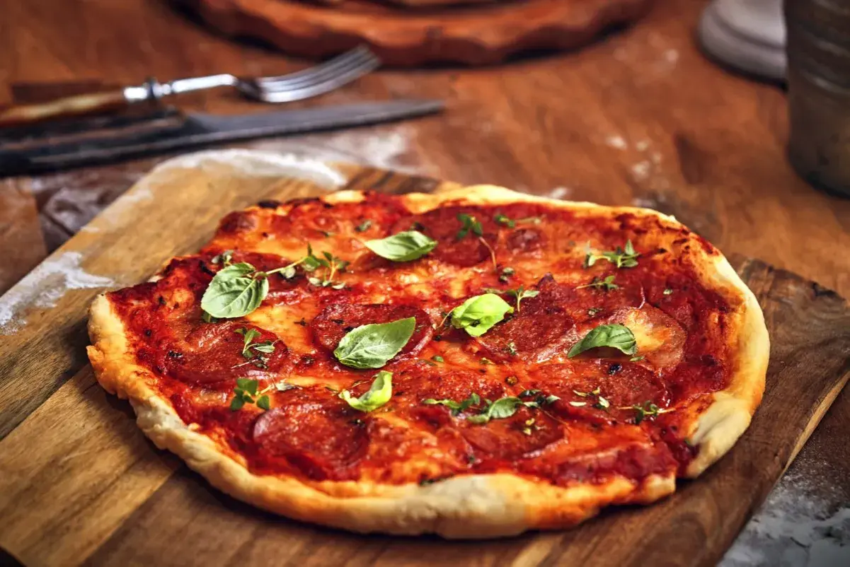 Pikantna spianata calabrese na pizzy, ozdobiona świeżą bazylią i ziołami, czeka na talerzu.