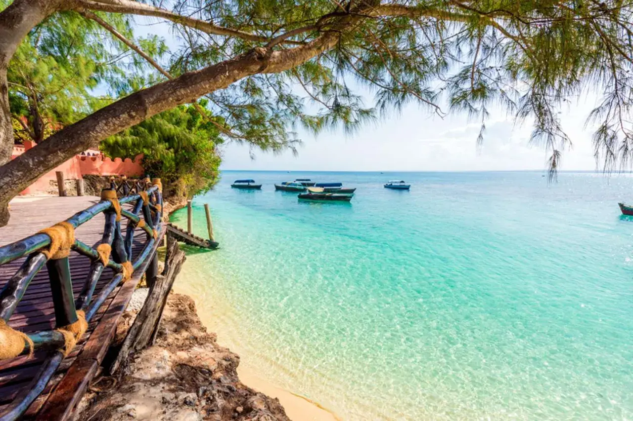 Drewniana kładka prowadzi do turkusowej wody, gdzie kołyszą się łodzie. Idealny widok na Zanzibar w czerwcu.