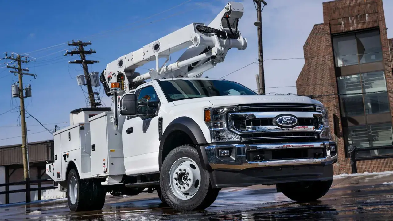 Biały Ford F650 z podnośnikiem koszowym gotowy do pracy przy liniach energetycznych.