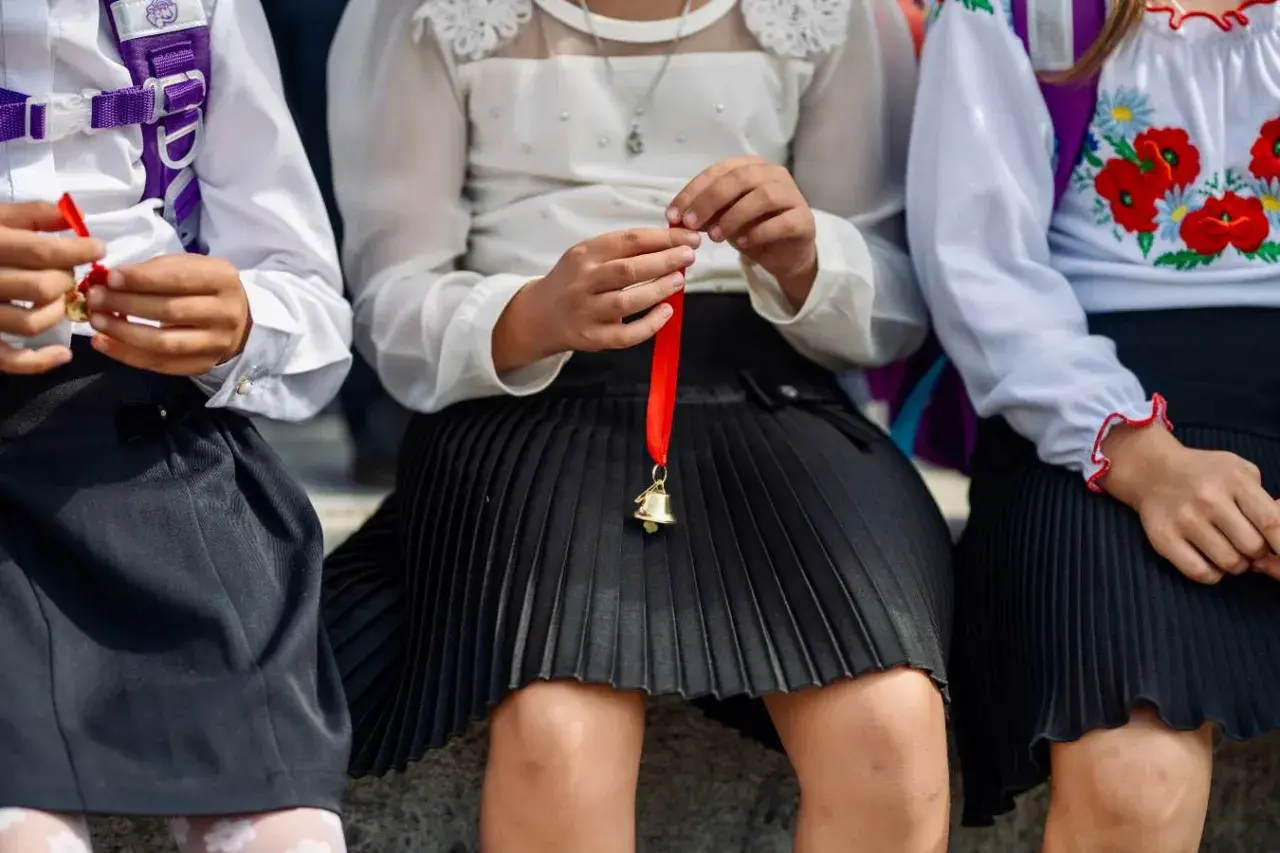 Trzy dziewczynki w szkolnych strojach, jedna trzyma dzwoneczek na wstążce. Czy w klasie 1-3 są świadectwa z paskiem?