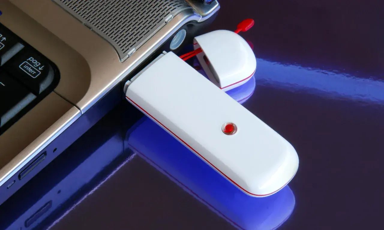 Biały modem USB podłączony do laptopa, umożliwiający komórkową transmisję danych.