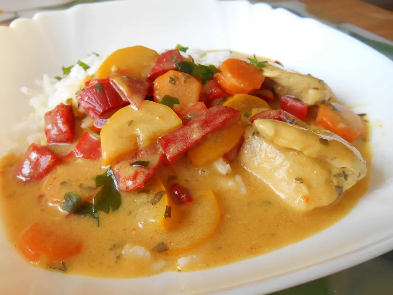 Kurczak curry z warzywami: kawałki kurczaka w kremowym sosie z papryką, marchewką i cukinią, podane z ryżem.