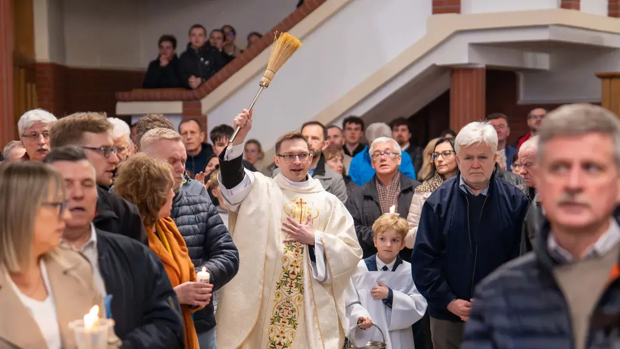Kapłan błogosławi wiernych podczas liturgii Wielkiej Soboty, unosząc kropidło. W tłumie widać ludzi z zapalonymi świecami.