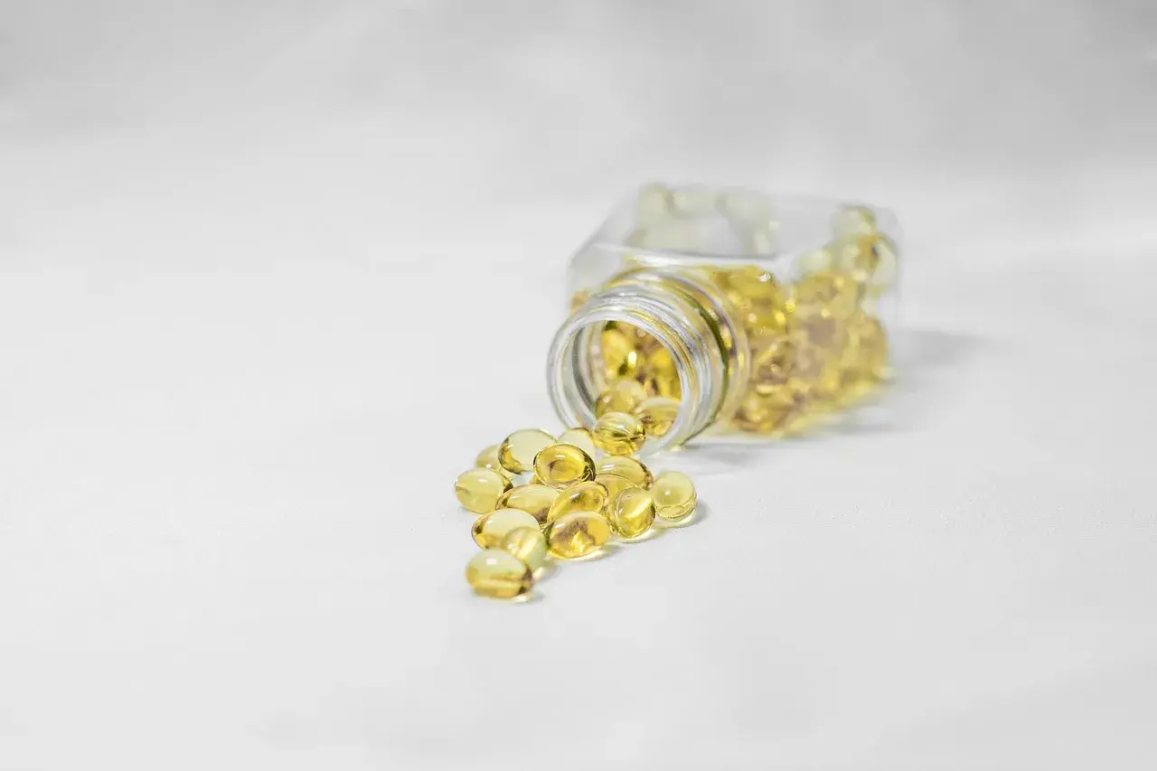 Żółte kapsułki, być może suplementy z kwasem fosfatydowym, wysypują się z przezroczystego słoiczka na białe tło.