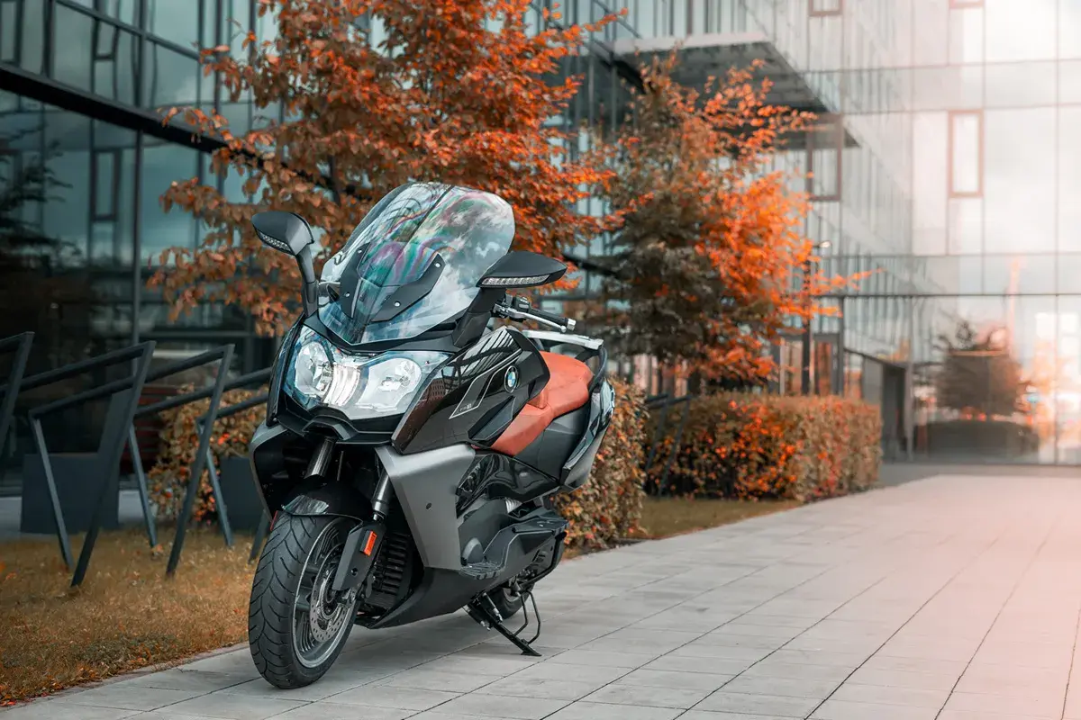 Skuter BMW C650 GT z brązowym siedzeniem na tle nowoczesnego budynku i jesiennych drzew. Dane techniczne tego modelu są imponujące.