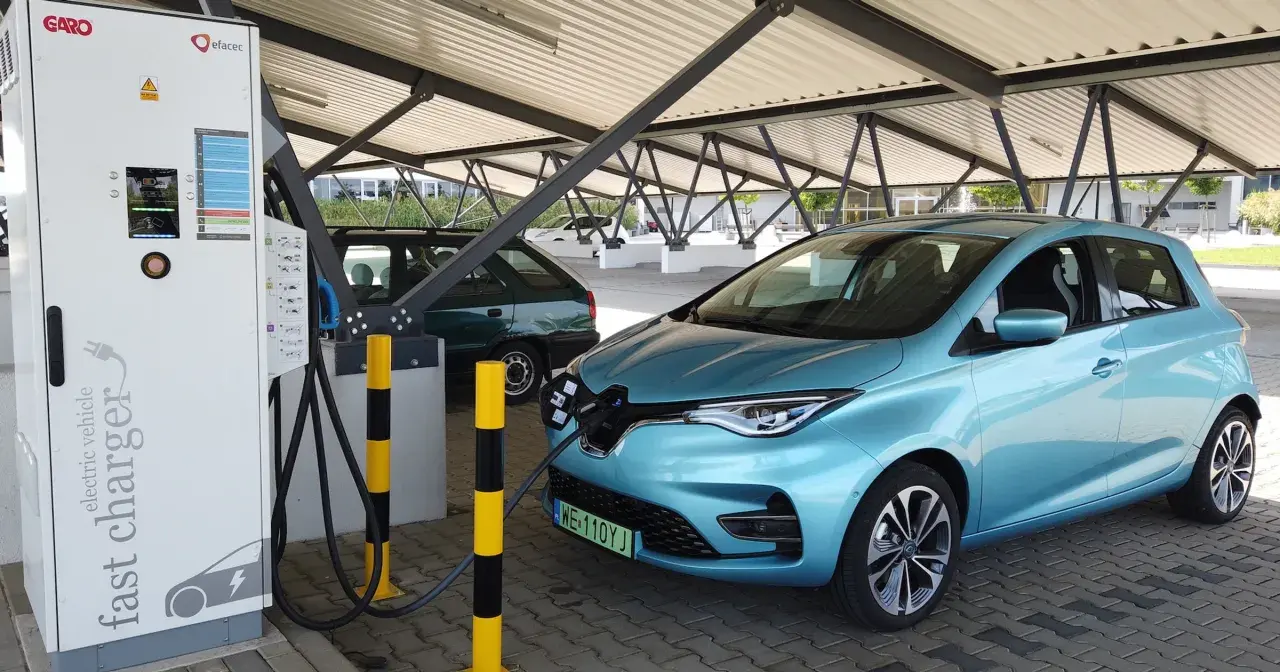 Błękitny Renault Zoe podłączony do ładowarki na parkingu pod zadaszeniem.