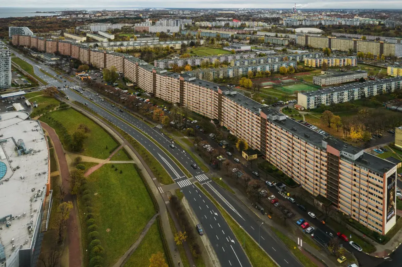 Widok z lotu ptaka na najdłuższy blok w Europie, rozciągający się wzdłuż ruchliwej drogi i otoczony zielenią oraz innymi budynkami mieszkalnymi.