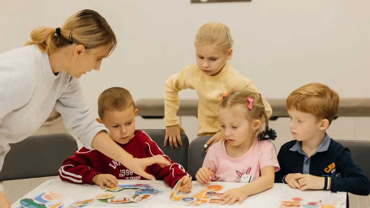 Nauczycielka pomaga dzieciom układać obrazki. Czy przedszkole może wypisać dziecko? Dzieci uczą się przez zabawę.