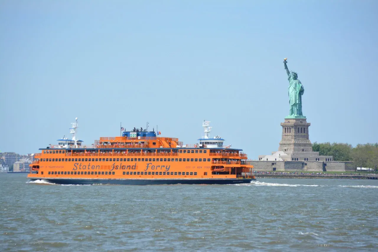 Pomarańczowy prom Staten Island Ferry płynie obok Statuy Wolności.