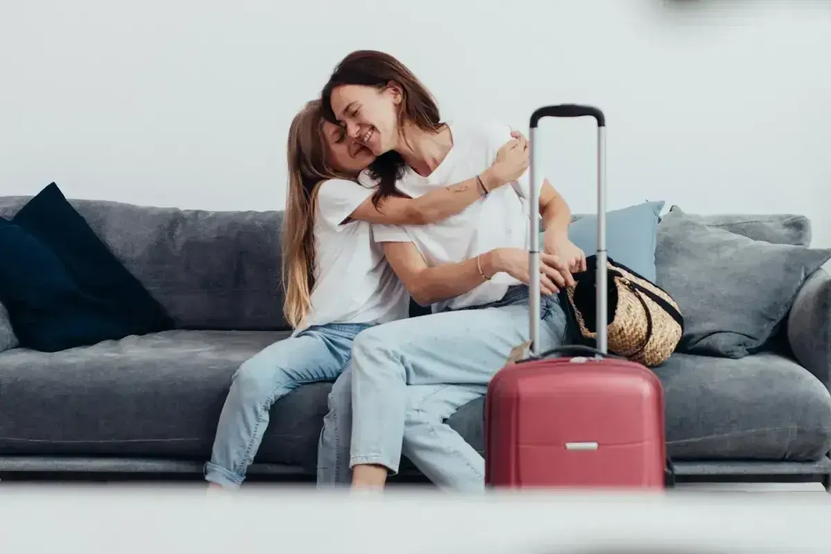 Mama i córka przytulają się na kanapie, obok walizka. Wszyscy, którzy chcą zameldować się w hotelu, mogą tu poczuć się jak w domu.