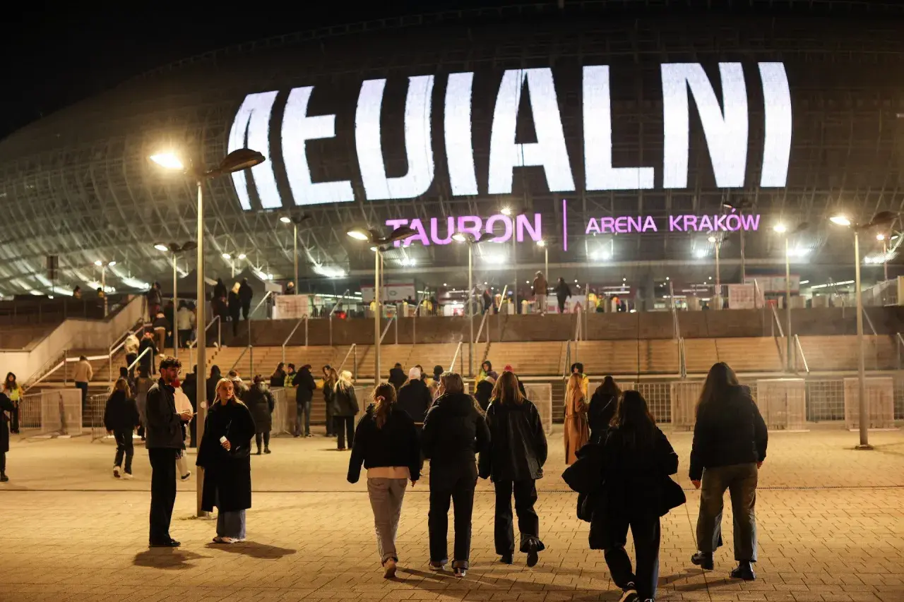 Tłum ludzi zmierza do Tauron Areny Kraków na koncert. Wielki napis na dachu obiektu zapowiada wydarzenie. To prawdziwy **rush w Polsce**!