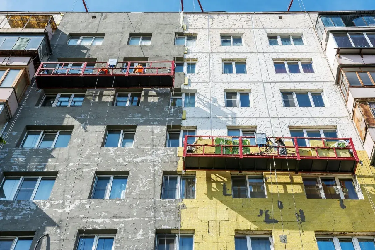 Remont bloku mieszkalnego w toku. Czy remont mieszkania trzeba zgłaszać? Pracownicy na rusztowaniach ocieplają budynek.