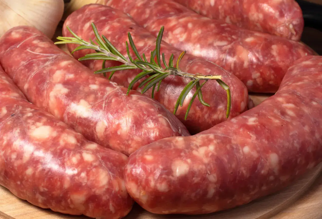 Salsiccia co to? Surowe kiełbaski wieprzowe, przyprawione ziołami, leżą na desce.