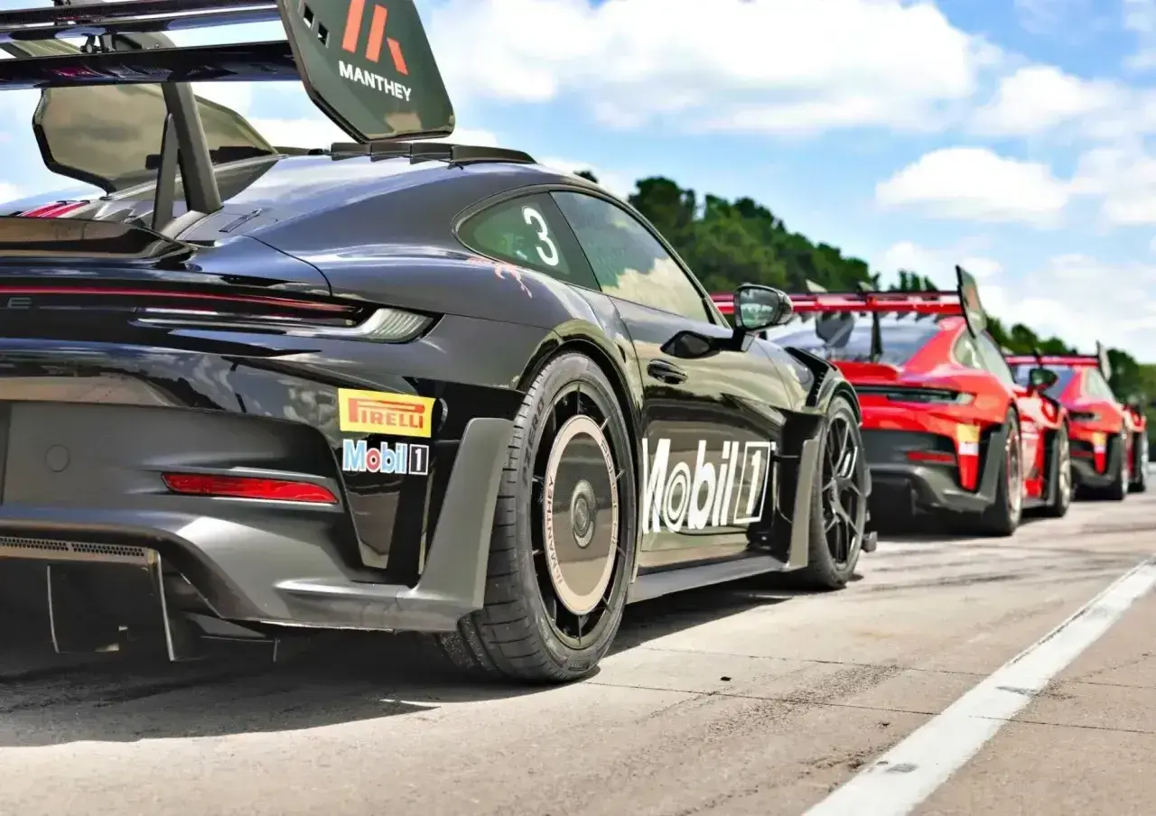 Czarny Porsche GT3 RS z numerem 3 i logo Manthey na skrzydle, gotowy do wyścigu obok czerwonych samochodów.