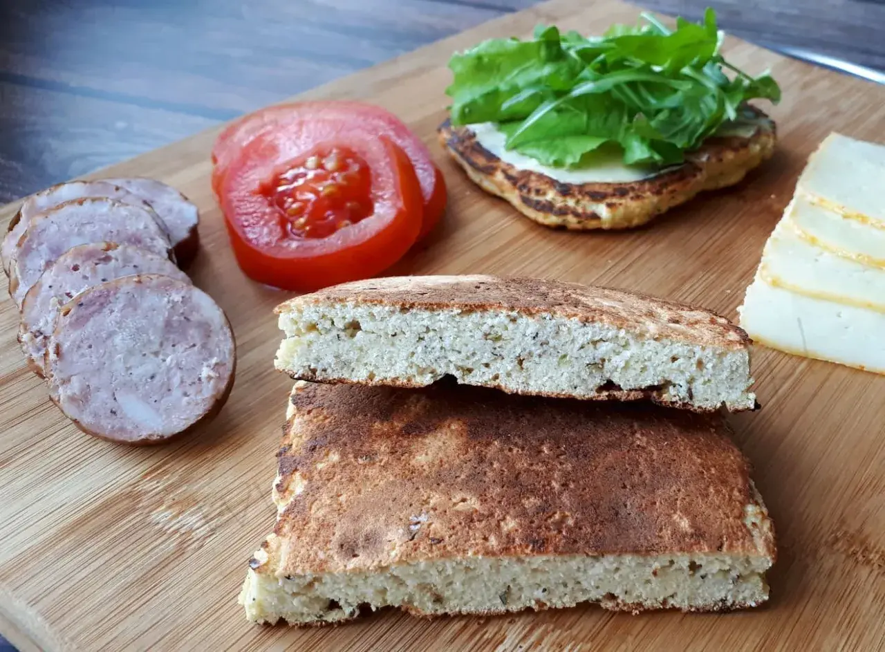 Chleb keto, plasterki kiełbasy, pomidor i ser na desce. Idealne składniki na keto kanapkę.