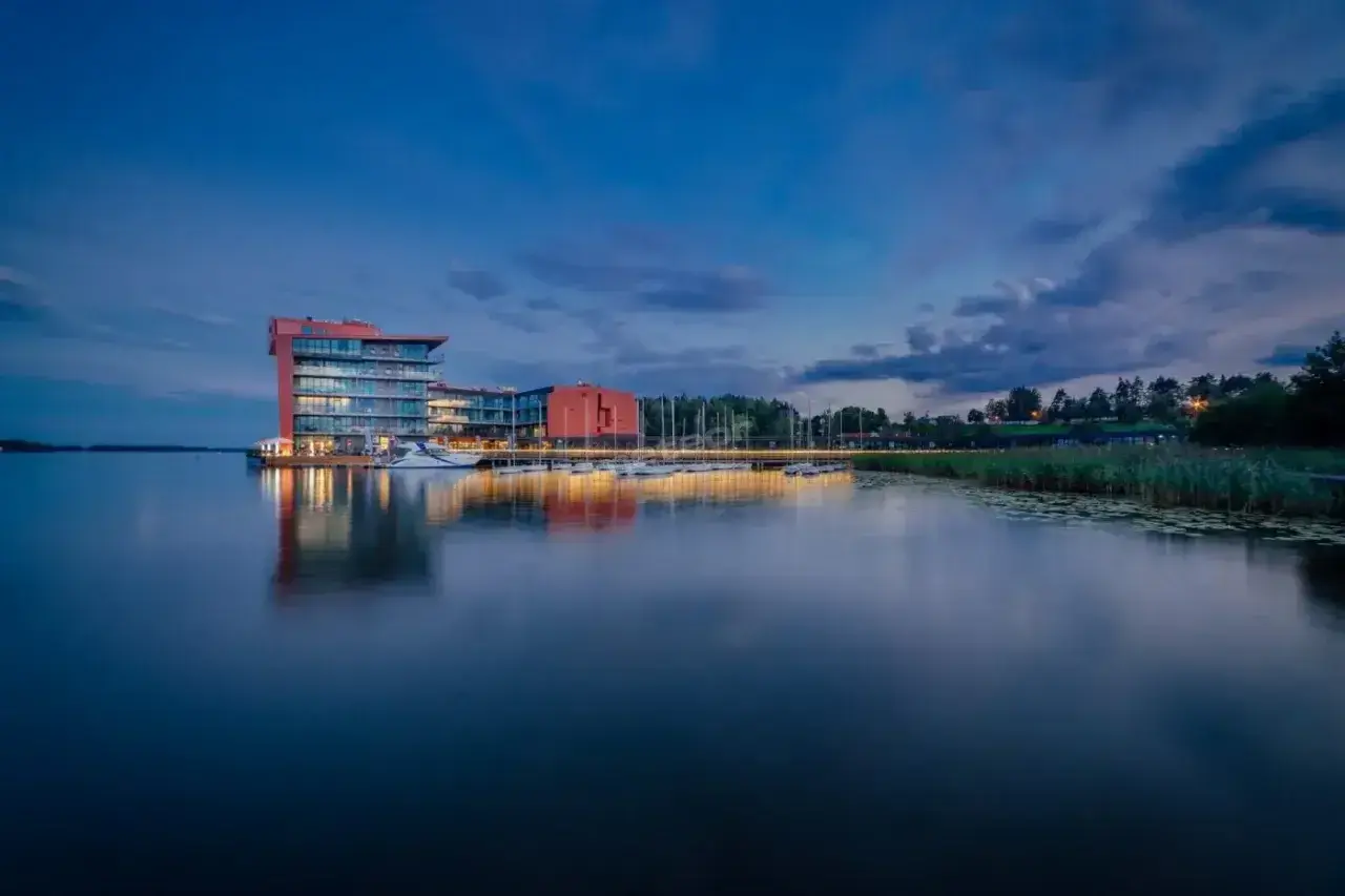 Nowoczesny hotel na ptasiej wyspie, otoczony spokojną wodą i zielenią, z łodziami przy pomoście.