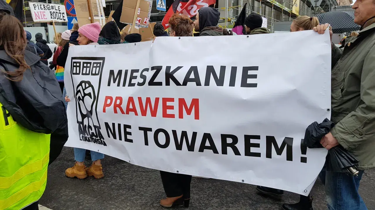 Protestujący niosą transparent "Mieszkanie prawem nie towarem!", domagając się ustaw chroniących lokatorów.