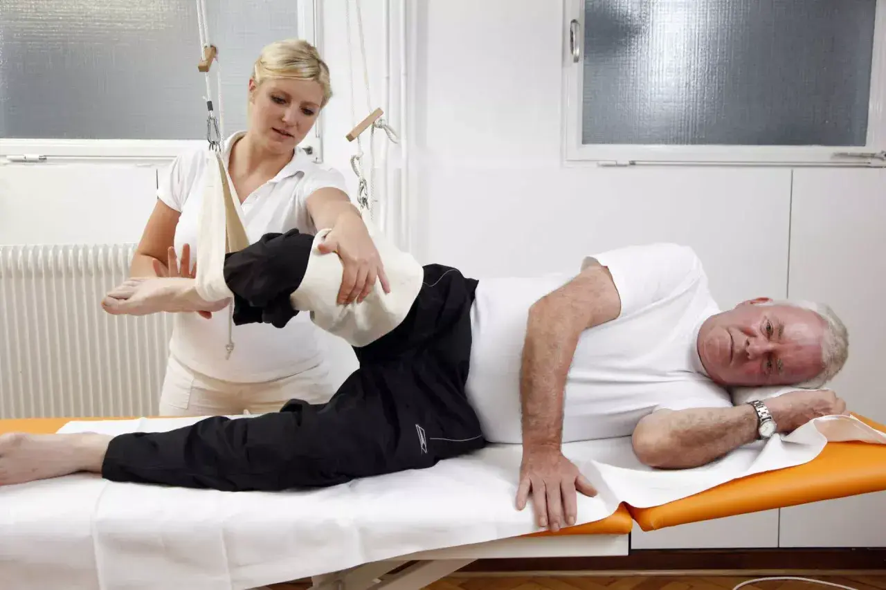 Physiotherapeutin hilft Mann bei Übungen. Die Krankenkasse bezahlt solche Behandlungen zur Genesung.
