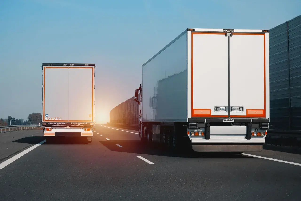 Dwa białe tiry jadą autostradą. Na jednym z nich widać znak zakazu wyprzedzania dla ciężarówek.
