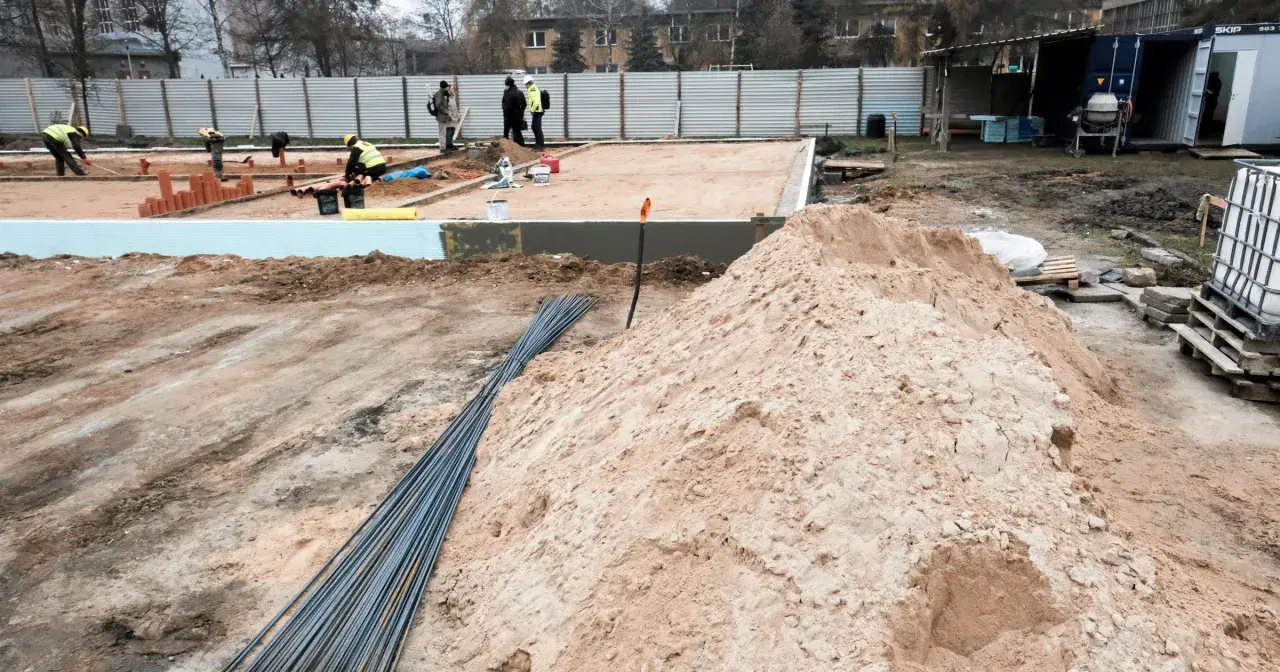 Budowa w marcu 2026. Działka z uregulowanym stanem prawnym, przygotowana pod fundamenty. Piasek, zbrojenie i pracownicy na placu budowy.