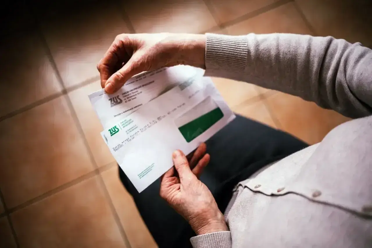 Dłonie trzymają kopertę ZUS. W środku dokumenty dotyczące 13 emerytury netto.
