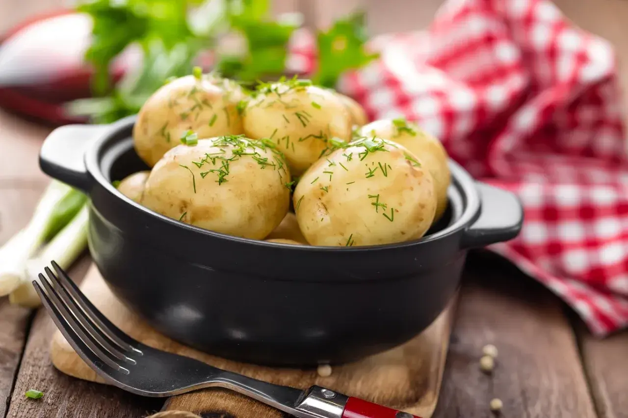 Gotujesz ziemniaki na ból ucha? Te młode ziemniaczki, posypane koperkiem, wyglądają apetycznie. Obok widelec i czerwono-biała serwetka.