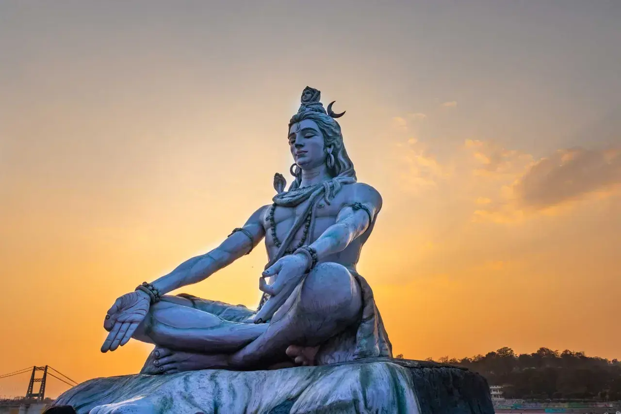 Eine riesige Statue von Shiva sitzt in meditativer Haltung vor einem warmen Sonnenuntergang.