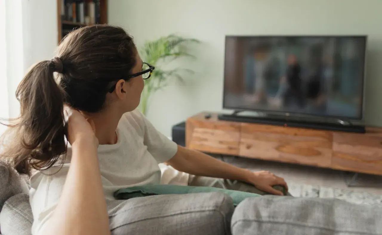 Kobieta w okularach relaksuje się na kanapie, oglądając telewizor. Idealna jaka odległość od telewizora 65 cali?