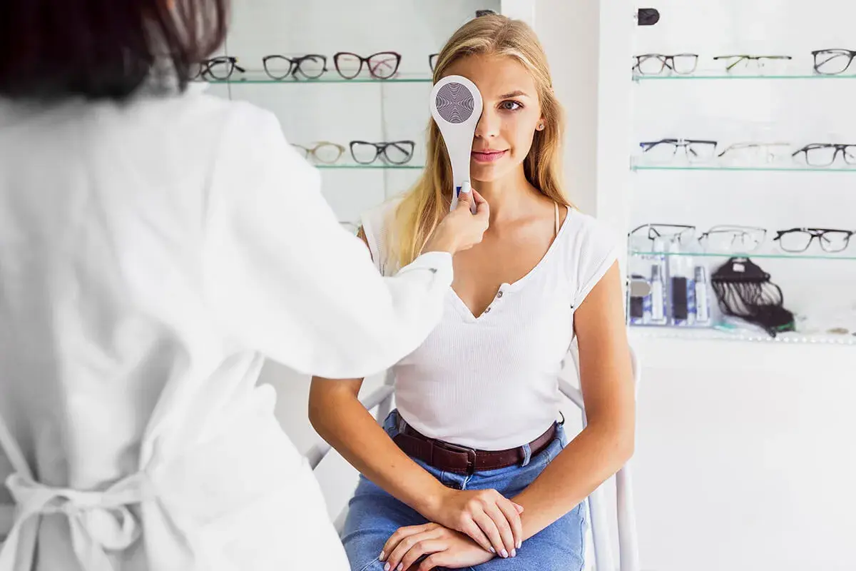Młoda kobieta przechodzi badanie wzroku. Optometrysta zasłania jej jedno oko przyrządem do cover testu.