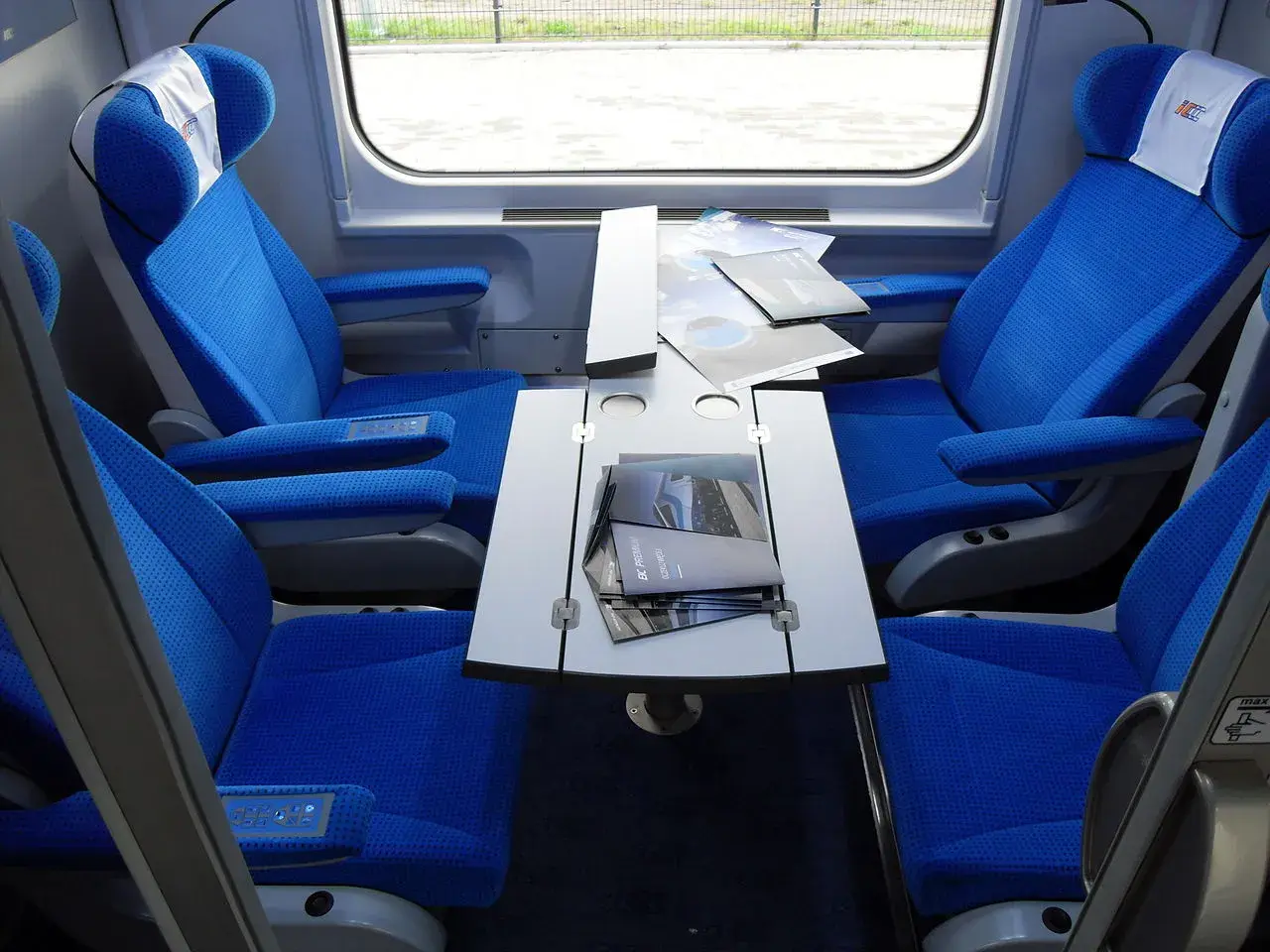 Wnętrze wagonu przedziałowego z wygodnymi, niebieskimi fotelami i stolikiem.