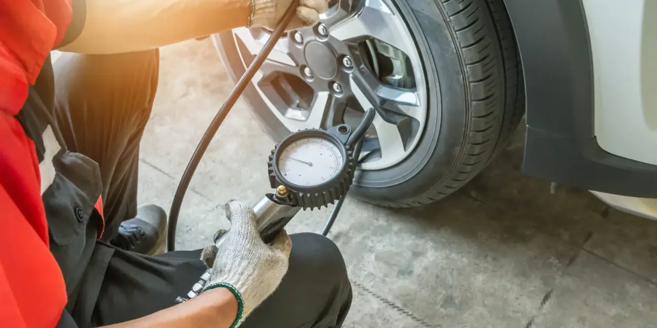 Controllo pressione gomme: il manometro indica pressione gomme troppo alta. Un meccanico con guanti sta verificando la pressione di un pneumatico.