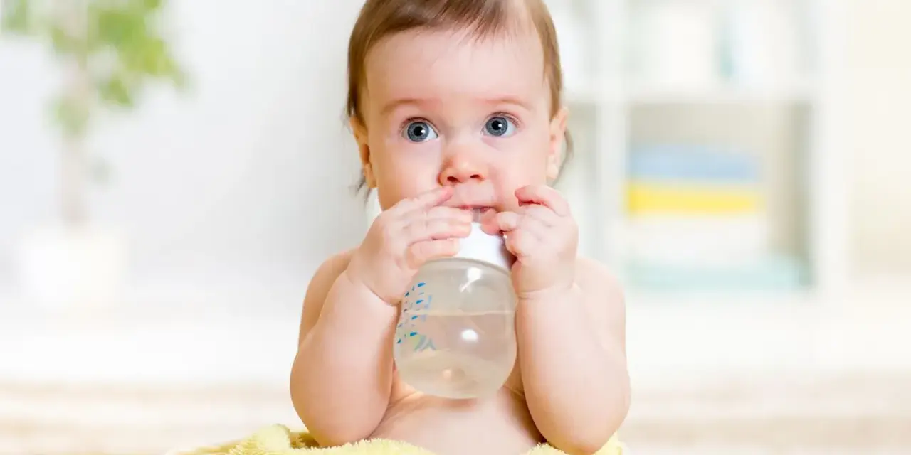 Ein süßes Baby mit blauen Augen hält eine Flasche und trinkt. Es scheint, als ob dieses Baby zu viel trinkt, aber es genießt jeden Schluck.