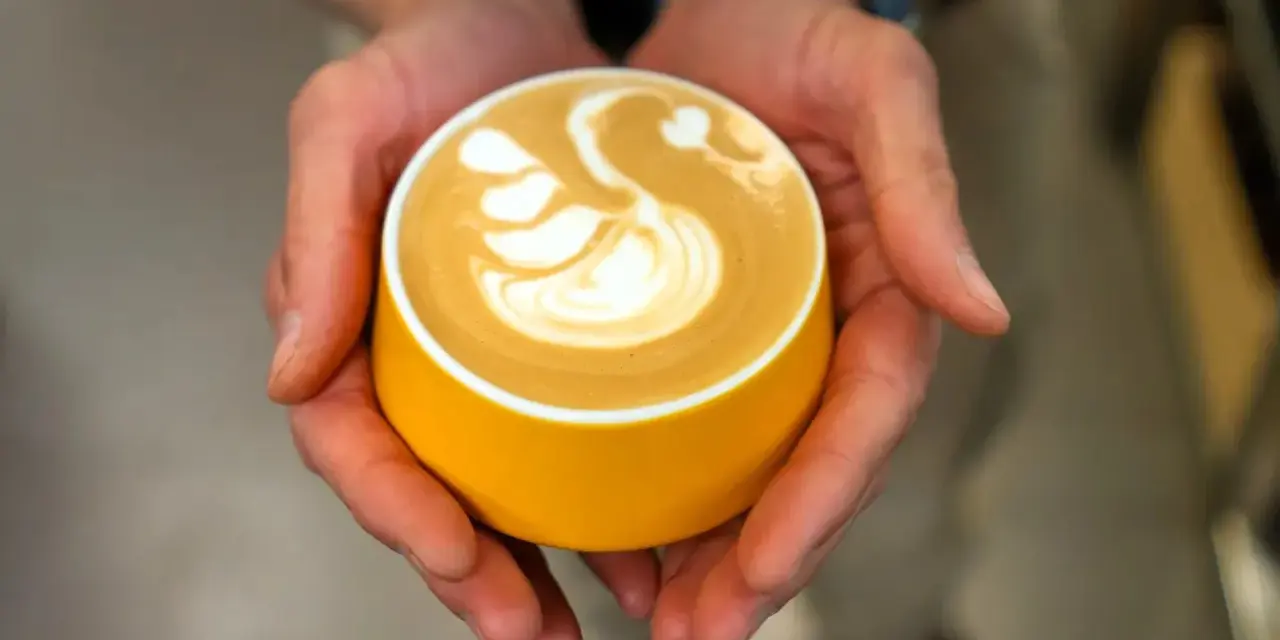 Dłonie trzymają żółtą filiżankę z kawą, na której widnieje wzór łabędzia. Zastanawiasz się, ile kofeiny ma espresso?