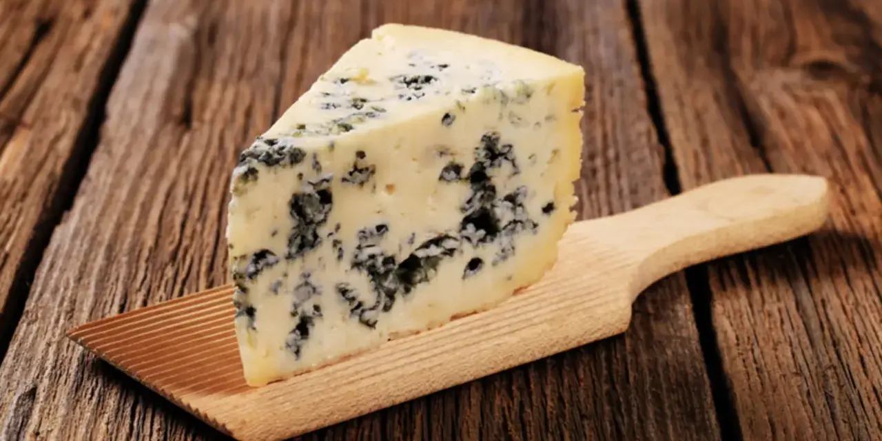 Ein Stück Blauschimmelkäse, perfekt für eine cremige blue cheese sauce, liegt auf einem Holzbrett.